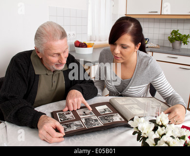 Una giovane donna guarda a un album di foto con i cittadini anziani, Eine junge Frau schaut mit Senioren ein Fotoalbum un Foto Stock