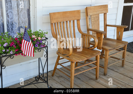 Due sedie di legno sul vecchio portico anteriore con i fiori e la bandiera americana Foto Stock