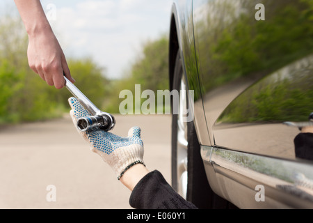 Donna che consegna a un socket o la chiave di un meccanico che lavora sotto la sua automobile dopo che esso ha abbattuto a lato Foto Stock