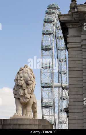 La Coade leone di pietra a guardia della estremità meridionale del Westminster Bridge con il London Eye sullo sfondo Inghilterra Foto Stock