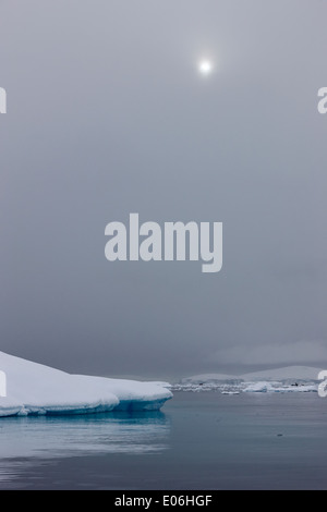 Rottura sole attraverso la nebbia e le nubi sulla coperta di neve ghiaccio ripiano che cadono in mare a Fournier Bay Antartide Foto Stock