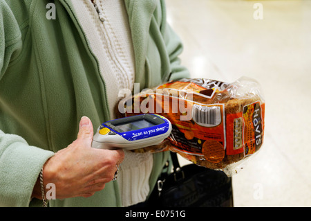 Una donna anziana con le mani in mano la scansione di una pagnotta di pane in Tesco scansione come si acquista Foto Stock