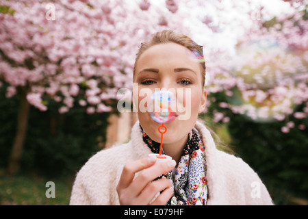 Ritratto di giovane e bella donna soffiare bolle al parco. Bella femmina modello con bacchetta di bolla a spring blossom garden. Foto Stock