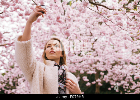 Giovane e bella signora fotografare la natura con il suo telefono cellulare. Piuttosto giovane donna a primavera sbocciano i fiori park scattare fotografie.