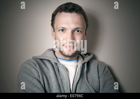 Sorridente giovane uomo caucasico in grigio giacca sportiva con il cofano Foto Stock