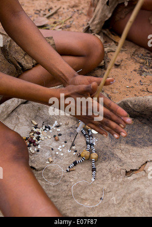 Donna boscimane facendo collane con uovo di struzzo Shell, Tsumkwe, Namibia Foto Stock