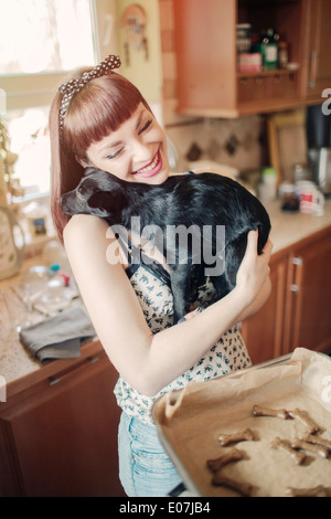 Giovane donna la cottura biscotti abbracciando il suo cane Foto Stock