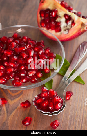 Fresche e mature i semi di melograno su una piastra di vetro.Due cucchiai. Sfondo di legno Foto Stock