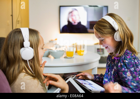 Felice sorelle ascoltando musica su digital compresse in salotto Foto Stock
