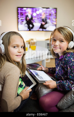 Ritratto di sorridere sorelle ascoltando musica su digital compresse in salotto Foto Stock