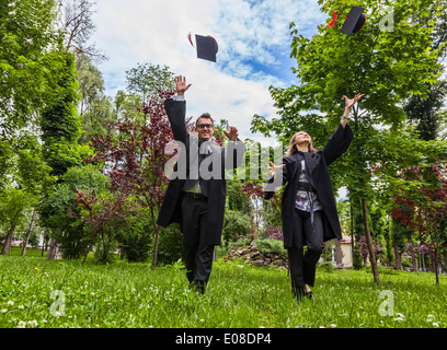 Coppia felice nel giorno di graduazione in esecuzione in un parco e gettando i loro cappelli. Foto Stock