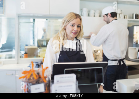 Ritratto di fiducioso proprietario femmina in piedi alla cassa in cafe Foto Stock