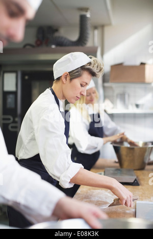 Vista laterale del panettiere femmina la cottura con i colleghi in cucina commerciale Foto Stock