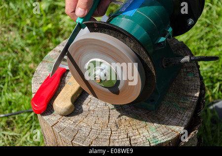 Affilatura a mano i coltelli con affilatore elettrico attrezzo su legno all'esterno log. Foto Stock