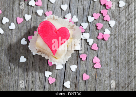 Petit Four decorate con cuore di marzapane in legno grigio Foto Stock