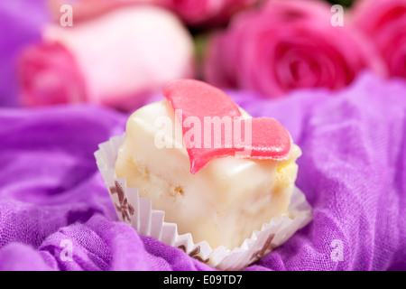 Petit Four decorate con cuore di marzapane sul panno viola Foto Stock