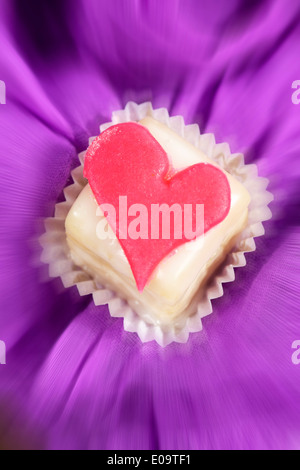 Petit Four decorate con cuore di marzapane sul panno viola Foto Stock