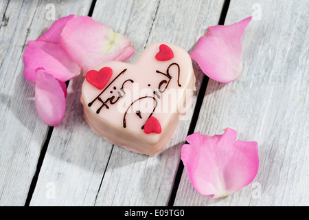 Petit Four con petali di rosa sul legno grigio Foto Stock