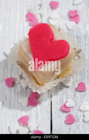 Petit Four decorate con cuore di marzapane in legno bianco Foto Stock