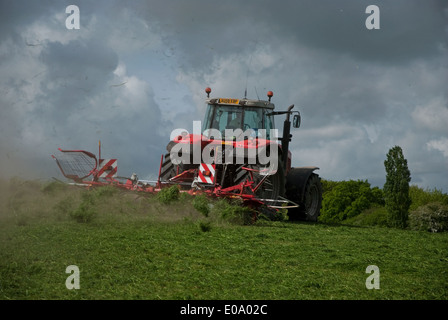 Il trattore gira erba secca per insilato in campagna britannica in primavera Foto Stock