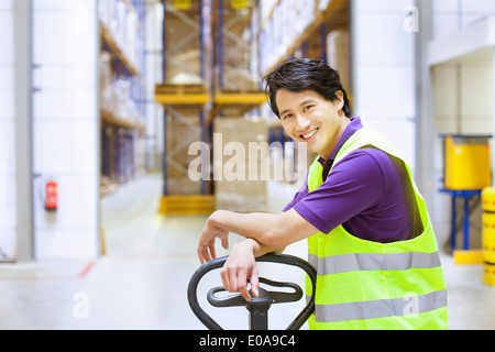 Ritratto di lavoratore di sesso maschile appoggiata sul martinetto pallet nel magazzino di distribuzione Foto Stock