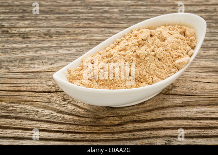 Radice di maca in polvere in una piccola ciotola di ceramica contro la venatura del legno Foto Stock