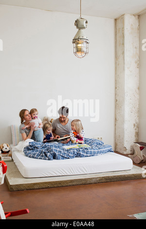 Famiglia con tre figlie la lettura di libri a letto Foto Stock
