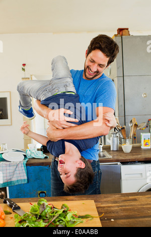 Padre azienda giovane figlio capovolto in cucina Foto Stock