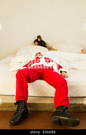 Ragazzo giovane vestito come babbo natale giacente sul letto Foto Stock