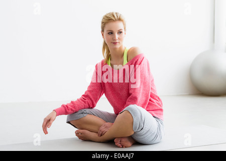 Giovane donna seduta sul tappetino di esercizio Foto Stock