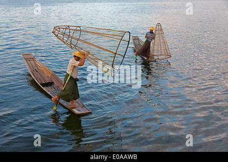 Pescatore Intha gamba barca a remi e pesce di colata net sul Lago Inle al tramonto, Stato Shan, Myanmar Foto Stock