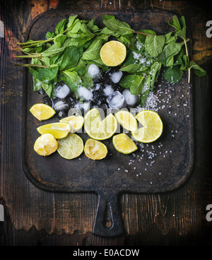 Ingredienti per il mojito (menta fresca, tigli, ghiaccio, zucchero) in ghisa nera scheda di taglio. Vista dall'alto. Foto Stock