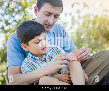 Padre amorevole mette un cerotto sul ginocchio del suo giovane figlio nel parco. Foto Stock