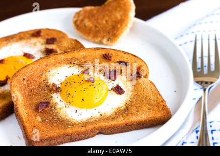 Uovo fritto in un cuore a forma di intaglio toast cosparso con pancetta briciole, incrinato pepe e timo Foto Stock