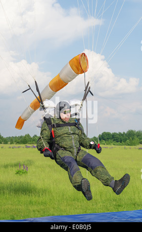 Un giorno con parachutist in aeroporto. Il paracadutista terre sotto il bianco paracadute. Atterraggio su un tappeto blu con piastra di bersaglio. Foto Stock