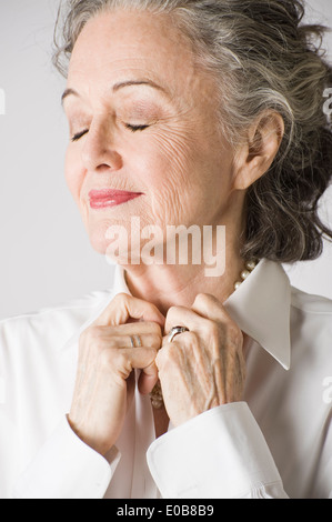 Ritratto di donna senior, mani sul collare a occhi chiusi Foto Stock