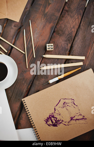 Immagine della tazza di caffè e oggetti per il disegno a mano e mani dell'artista con la penna sul blocco note Foto Stock