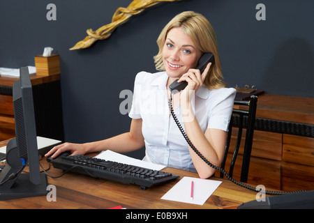 Hotel Receptionist utilizzando il computer e il telefono cellulare Foto Stock