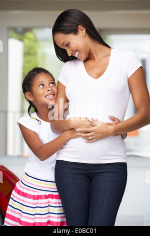 Figlia abbracciando la madre in stato di gravidanza Foto Stock