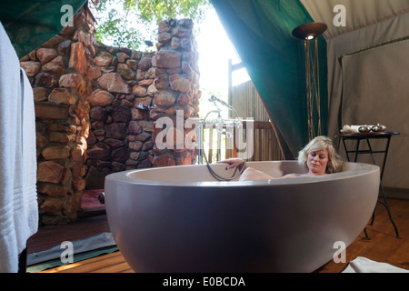 Donna bionda pan all'interno di una grande vasca ovale in un safari di lusso tenda, Botlierskop Game Lodge, Mosselbay, Sud Africa Foto Stock