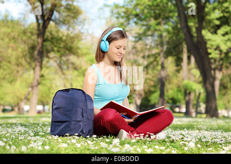 Studentessa leggendo un libro nel parco seduto su erba verde Foto Stock