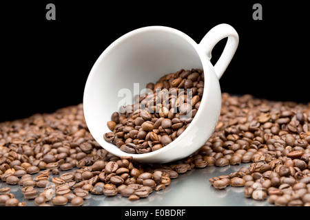 I chicchi di caffè versato all'esterno della tazza di caffè. Su sfondo nero. Foto Stock