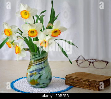 Bellissimi fiori grandi di narcisi in un vaso su un tavolo vicino al libro antico. Foto Stock