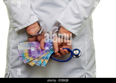 Un medico con Franco Svizzero di banconote e manette, Ein Arzt mit Schweizer Franken Geldscheinen und Handschellen Foto Stock