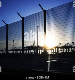 Area portuale recinto con sagome di gru di contenitore sotto la luce diretta del sole Foto Stock