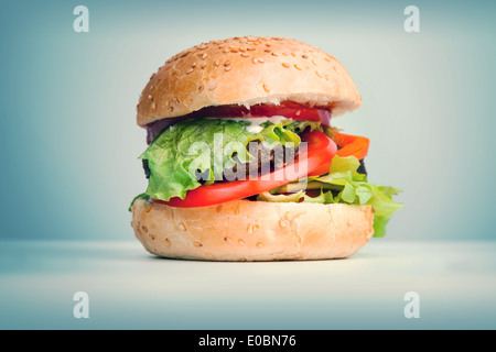 Grandi hamburger getta sul tavolo sopra lo sfondo blu, dai toni rétro foto Foto Stock