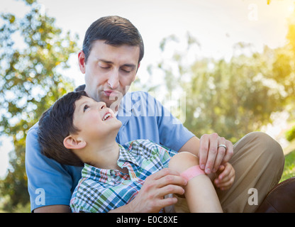 Padre amorevole mette un cerotto sul ginocchio del suo giovane figlio nel parco. Foto Stock