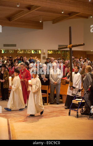 La Congregazione guarda come giovane derubato ministranti portano candele come essi conducono una processione portando una croce il Giovedì Santo a San Timoteo della Chiesa Cattolica, Laguna Niguel, CA. Nota pastore in rosso e assistente di pastore che porta la croce. Foto Stock