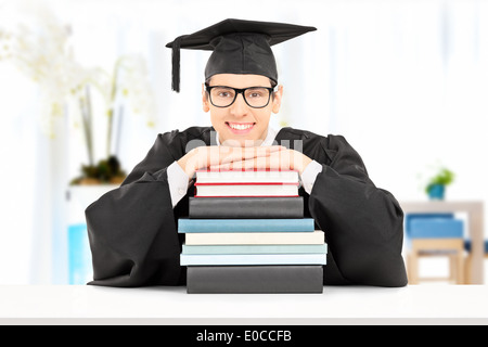 Studente maschio sorridente e appoggiata su una pila di libri a casa Foto Stock