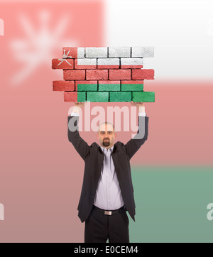 Imprenditore tenendo un grande pezzo di un muro di mattoni bandiera di Oman isolata sulla bandiera nazionale Foto Stock